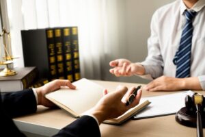 Two individuals in a legal office discuss documents, with law books and a gavel on desk.