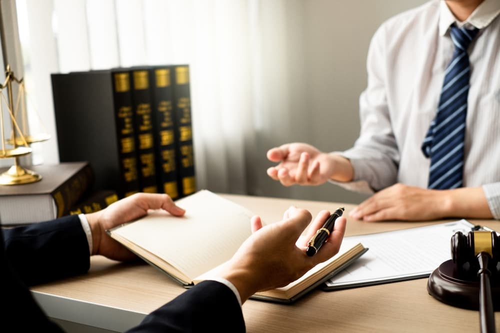 Two individuals in a legal office discuss documents, with law books and a gavel on desk.