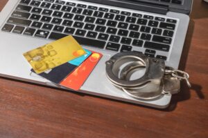 Handcuffs rest beside a laptop and credit cards, visually portraying identity theft and financial cybercrime.